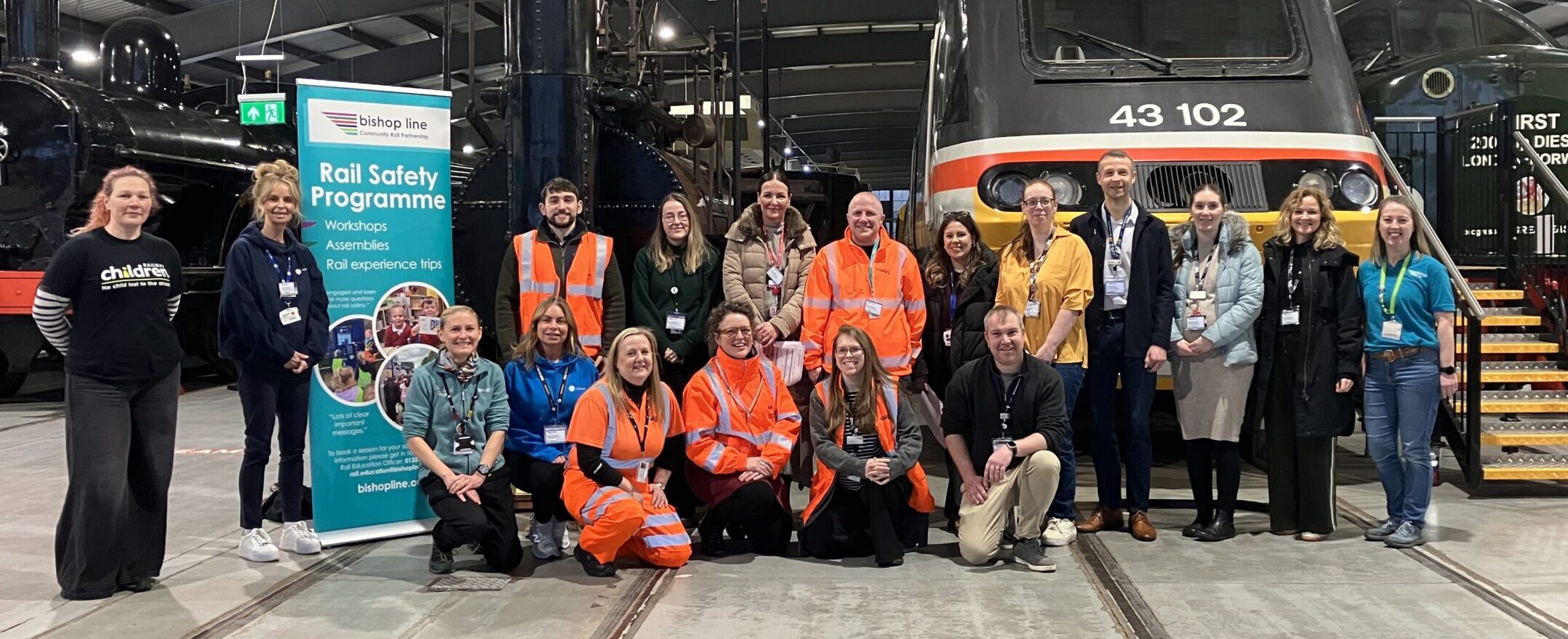 group of adults standing in front of trains inside a train museum