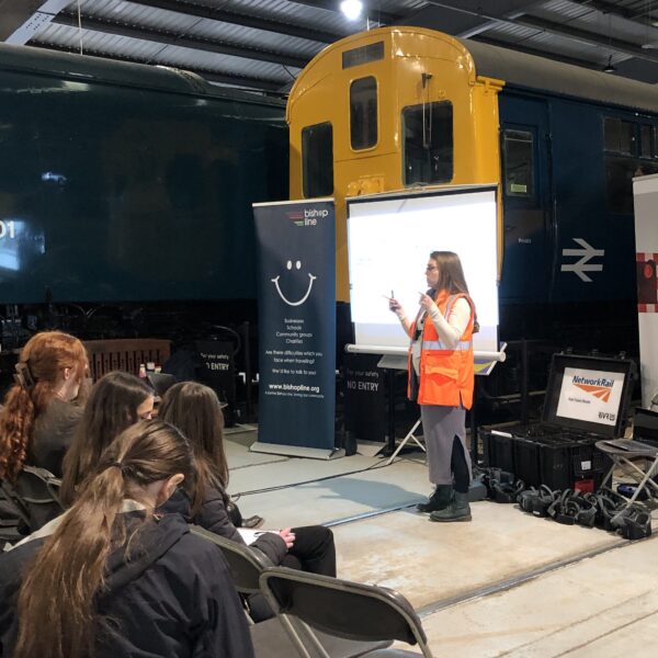 adult standing in front of a screen talking to young people, sitting in chairs inside a train museum.