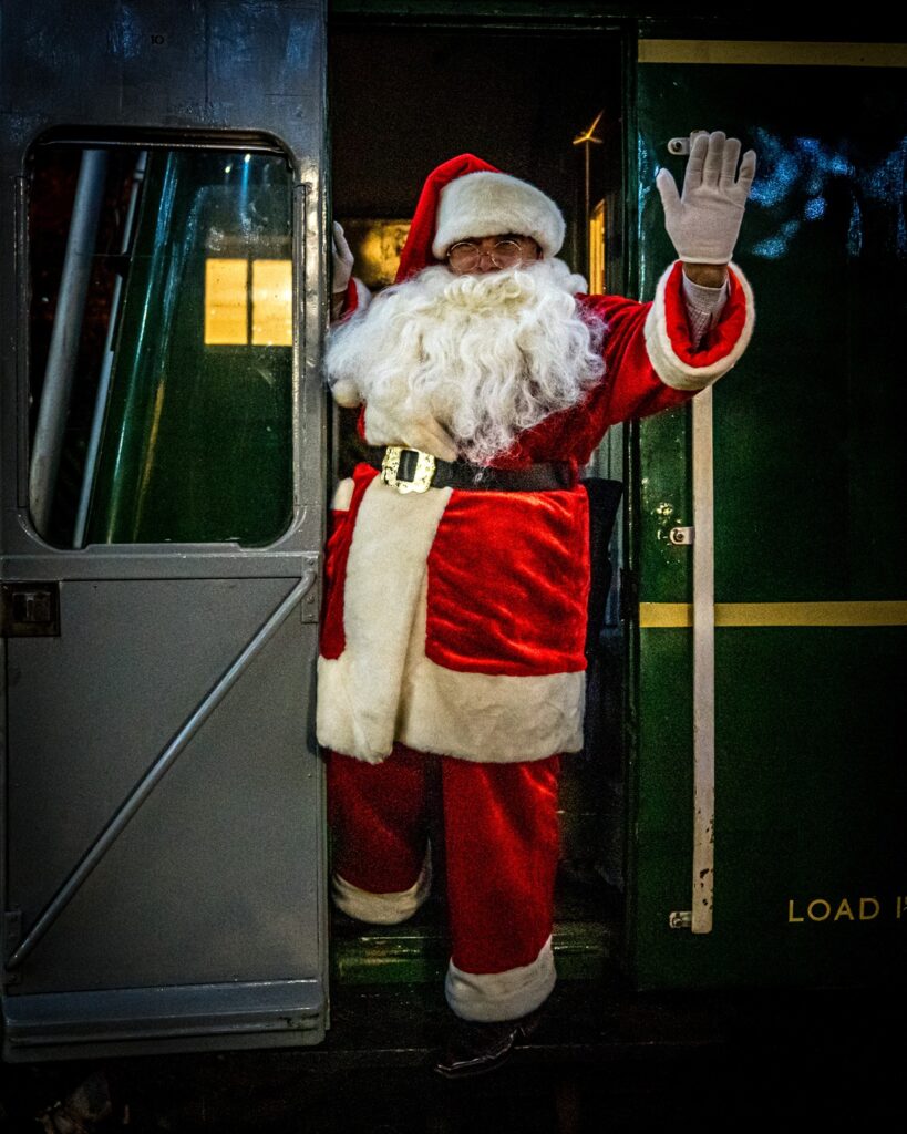 a person dressed as santa standing in the doorway of a train and waving.